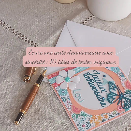 Carte d’anniversaire artisanale faite main posée sur une table, avec un stylo et des éléments fleuris – L’Atelier de Lili la souris