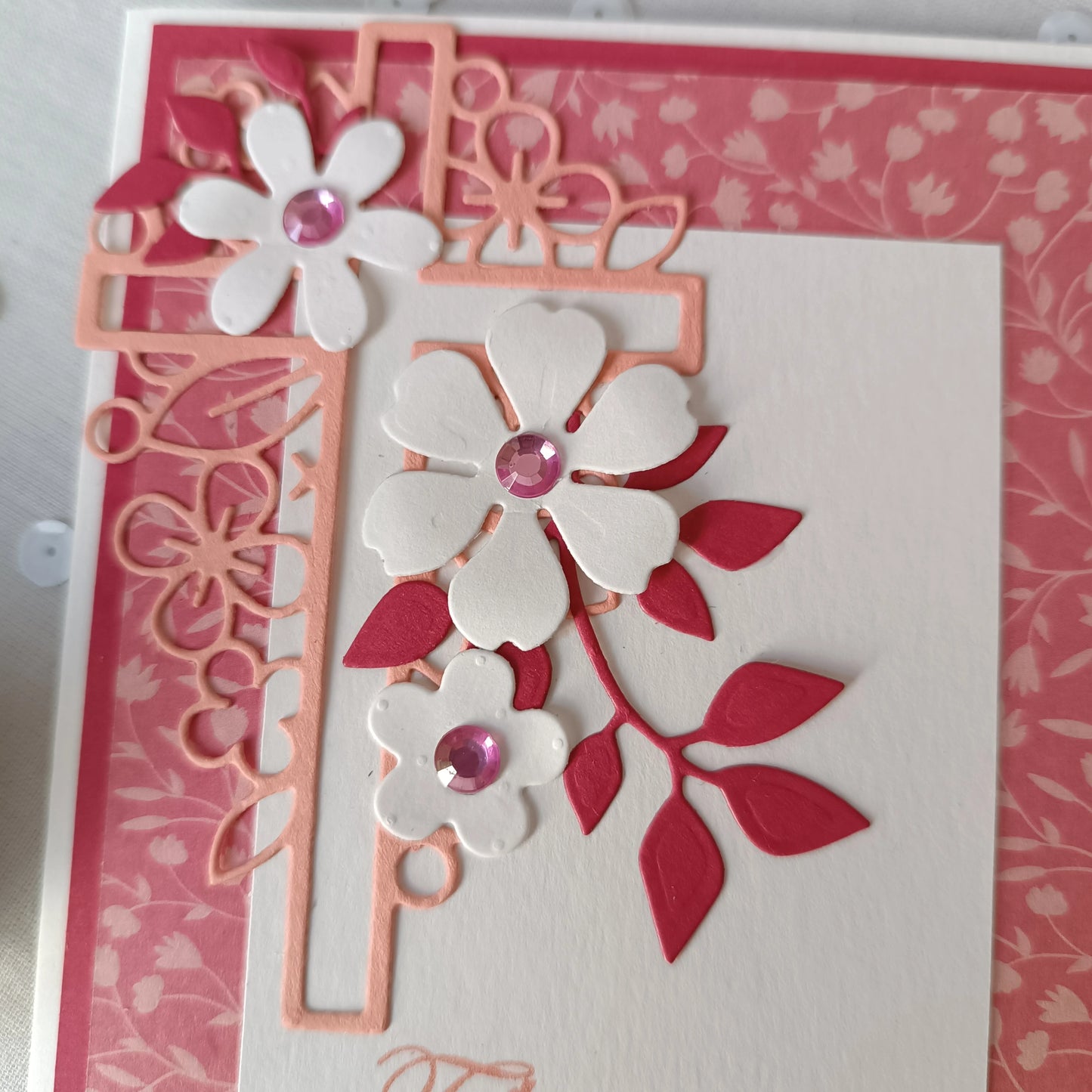Gros plan sur les fleurs blanches en relief et les strass roses de la carte de baptême