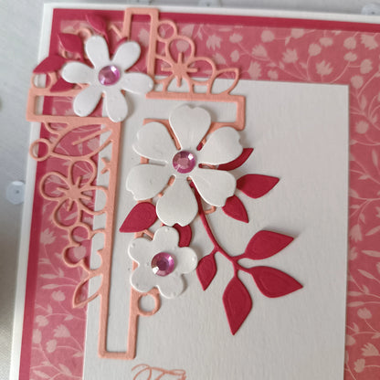 Gros plan sur les fleurs blanches en relief et les strass roses de la carte de baptême
