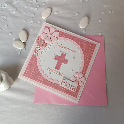 Carte de baptême rose personnalisable posée à plat, avec dragées, sequins et oiseau en céramique