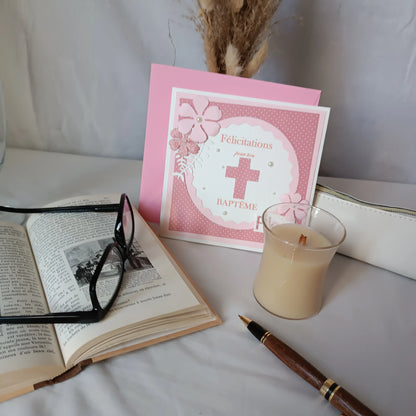 Carte de baptême rose personnalisable debout dans son enveloppe, avec livre ancien, lunettes et bougie
