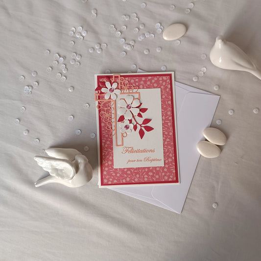 Vue plongeante de la carte de baptême rose posée sur un tissu, avec dragées et confettis décoratifs