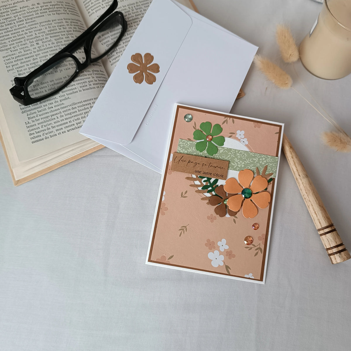 Carte de départ collègue abricot et vert sauge posée sur son enveloppe, avec livre ancien, lunettes et bougie