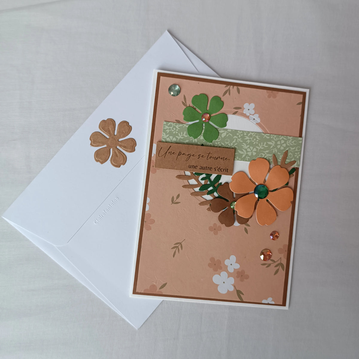 Carte de départ collègue artisanale abricot et vert sauge de L'Atelier de Lili la souris, posée sur son enveloppe blanche