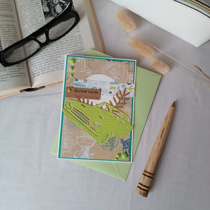 Vue en plongée de la carte de départ homme voiture posée sur son enveloppe, entourée d'une trousse, d'un livre ancien et de lunettes