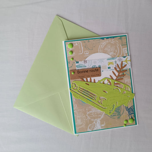 Carte de départ homme artisanale L'Atelier de Lili la souris, voiture vintage vert anis et tampons de voyage, posée sur son enveloppe vert tendre assortie
