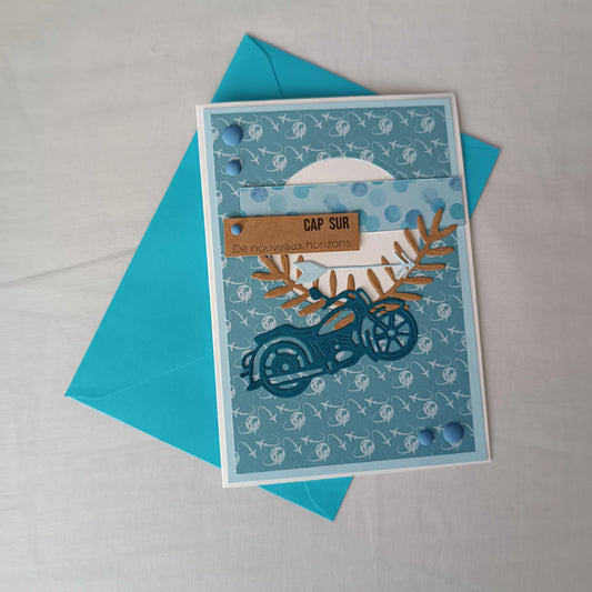 Carte de départ homme artisanale L'Atelier de Lili la souris, moto bleu sarcelle et motif avions, posée sur son enveloppe turquoise assortie