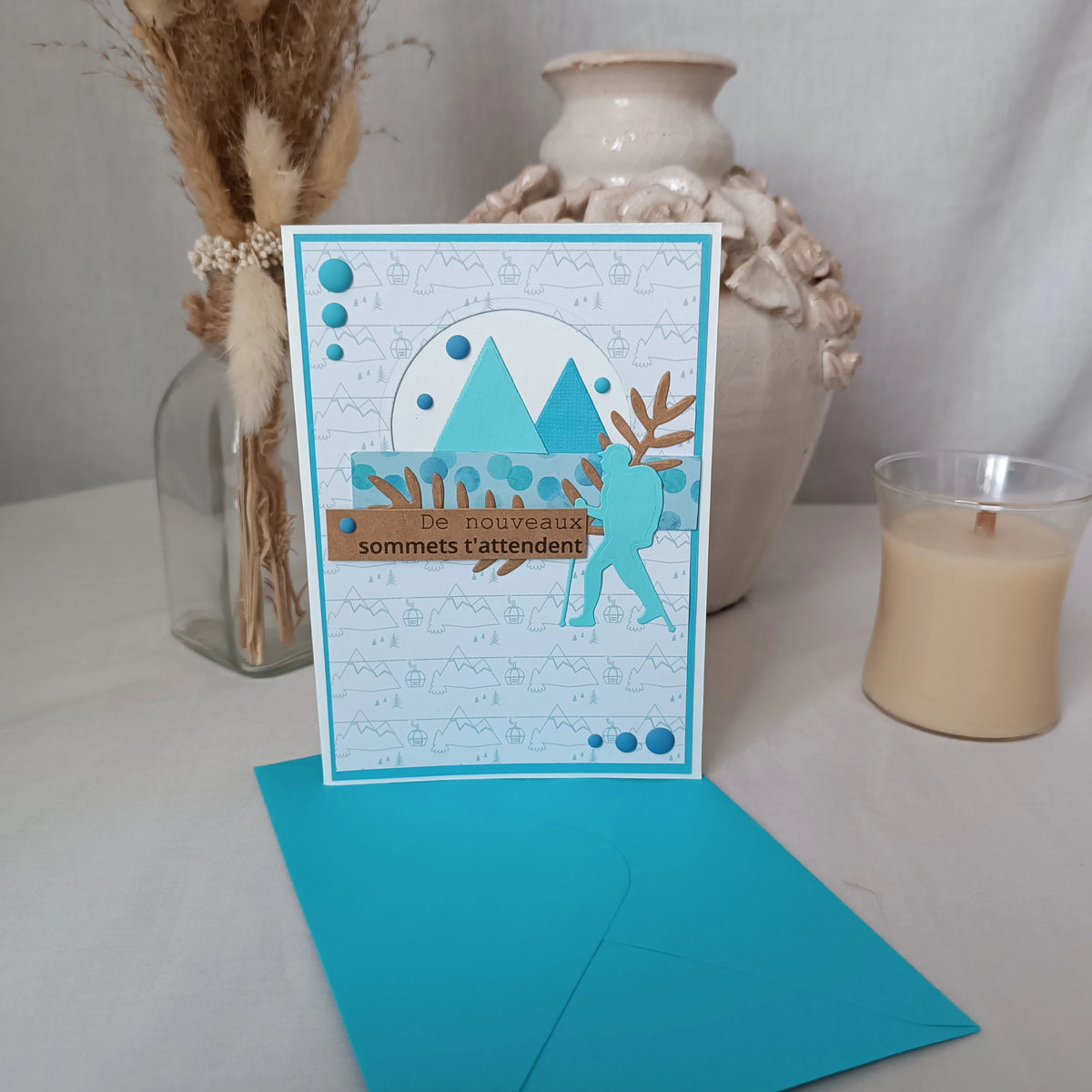 Carte de départ homme turquoise tenue debout devant un vase en céramique et une bougie, ambiance cosy
